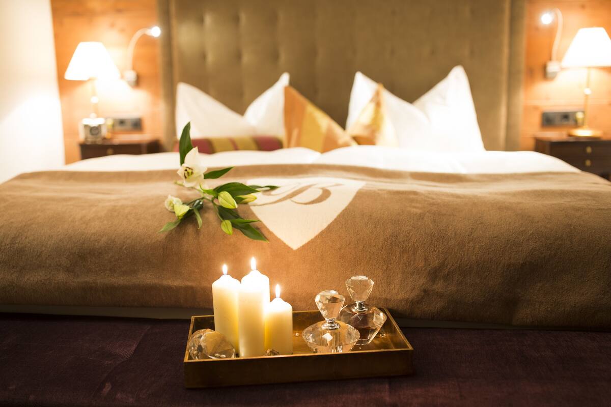 Una cama bien hecha con sábanas blancas, una bandeja con velas y cristalería decorativa.
