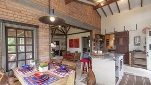 A spacious kitchen with a brick wall, wooden beams, and a large island with stools. - Vieja Hacienda (Imbituba)
