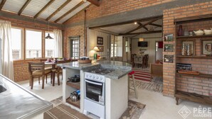 A kitchen with a built-in stove, wooden chairs, and a dining table. - Vieja Hacienda (Imbituba)
