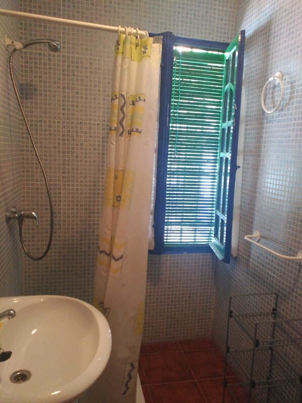 A bathroom with a shower, a window with blinds, a sink, and a towel rack. - Hostal San Bartolomé (Almagro)