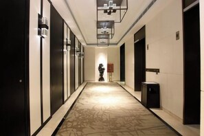 A hotel corridor with doors on both sides, a patterned carpet, and a wall-mounted light fixture. - Hotel Unic (NANJING)