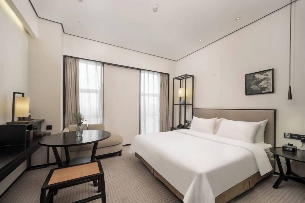 A hotel room with a bed, a desk, a chair, a small table, and a window.