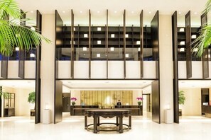 A modern hotel lobby with a reception desk, a large round table, and a high ceiling with recessed lighting. - Hotel Unic (NANJING)
