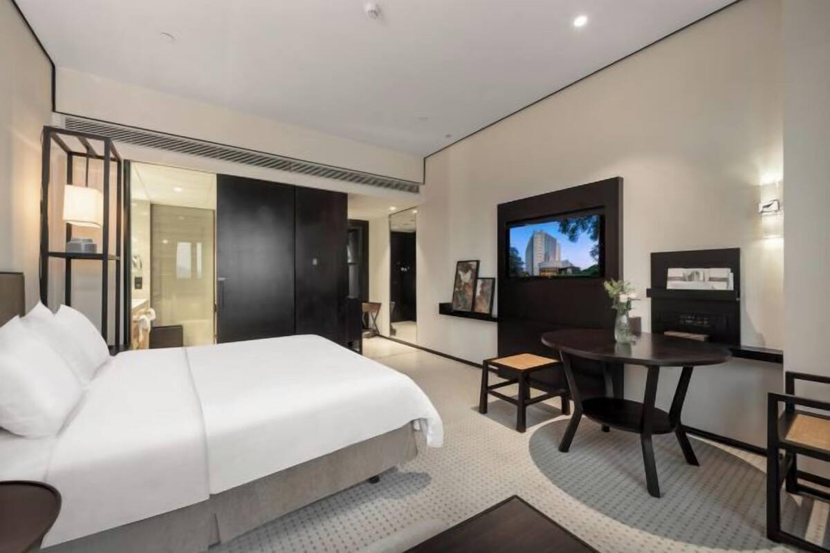 A hotel room with a bed, a TV, a small table with chairs, and a door leading to another room.