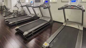 A row of treadmills in a gym with a wooden floor and a window in the background.