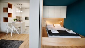 A modern bedroom with a bed, bedside table, and a view of a kitchen area. - CVO INN Cracow Old Town (Kraków)