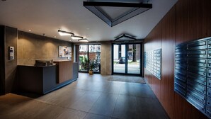 A modern reception area with a wooden reception desk, a digital information kiosk, and a wall of mailboxes. - CVO INN Cracow Old Town (Kraków)