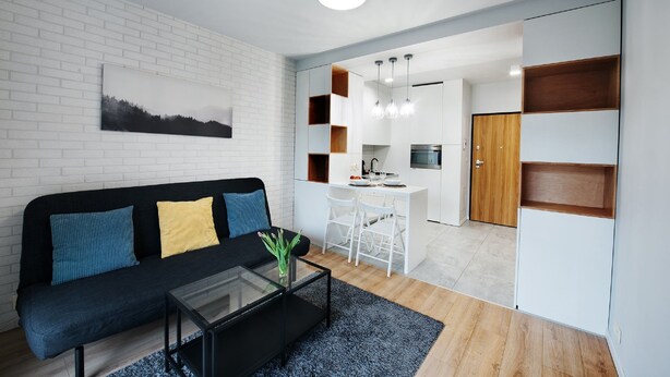 A modern living room with a black sofa, a glass coffee table, and a white brick wall. - CVO INN Cracow Old Town (Kraków)