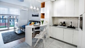 A modern kitchen with white cabinetry, a dining area with a glass table, and a view of the outside. - CVO INN Cracow Old Town (Kraków)