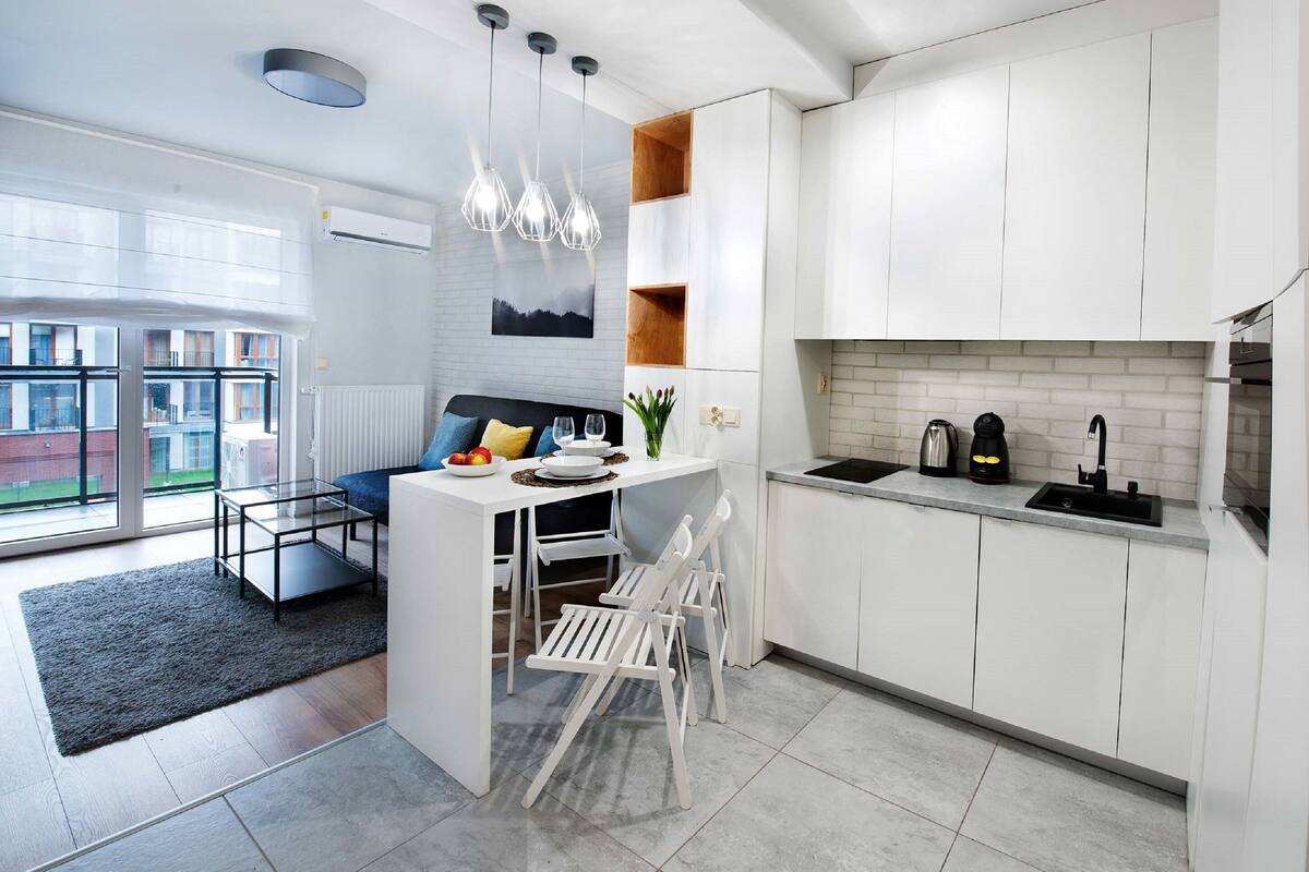 A modern kitchen with white cabinetry, a dining area with a glass table, and a view of the outside.