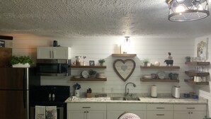 A kitchen with white cabinets, a stainless steel refrigerator, a microwave, and a sink. There are shelves with decorative items and a heart-shaped mirror on the wall. - “Lake Life” - Boat ramp here (Broaddus)