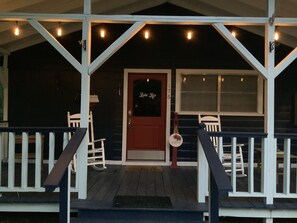 A porch with a red door, white railings, and string lights.