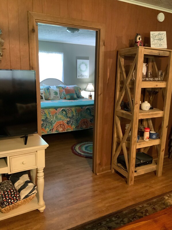 A room with a bed, a TV, a wooden shelf with glassware, and a welcome sign.