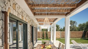 An outdoor patio with a stone wall, a wooden table with wicker chairs, and a hanging light fixture. - Gerakas Luxury Villas (Zakynthos)