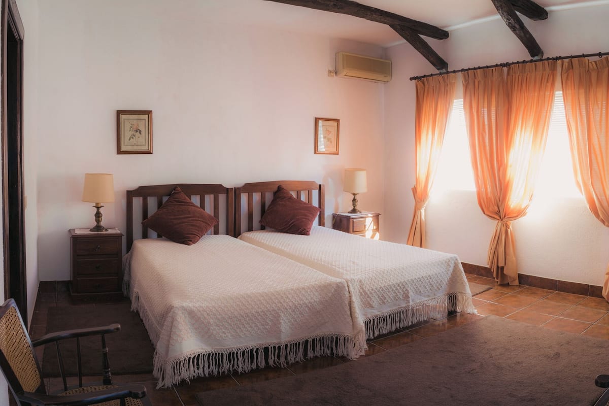 A double bed with a wooden headboard, two bedside tables with lamps, a chair, and a desk with a vase.