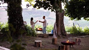 A couple toasting with wine glasses near a campfire in a forested area with a view of hills. - Quinta da Cumieira (Santa Marta de Penaguião)