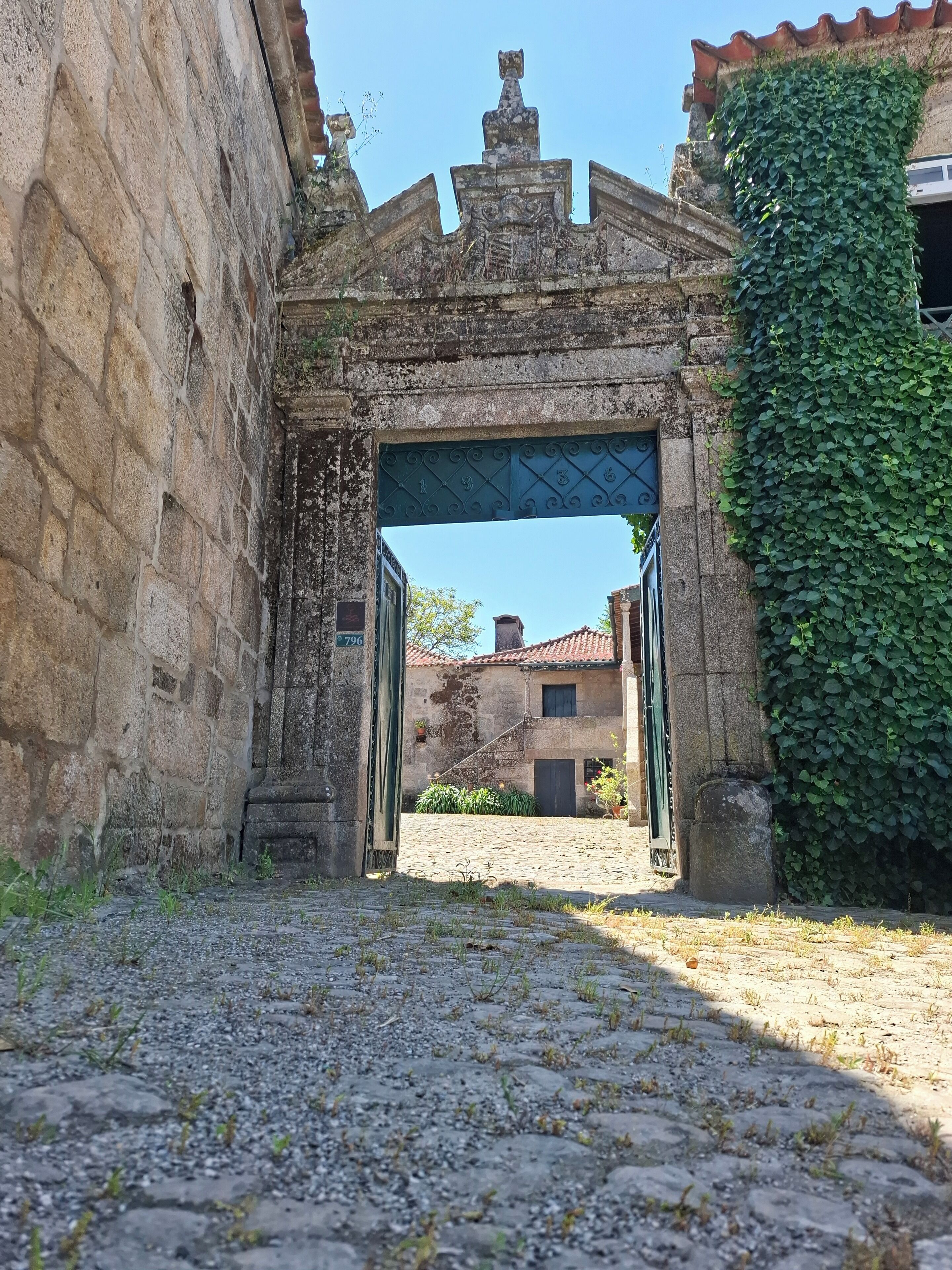 Un edifici antic de pedra amb una reixa metàl·lica i un camí empedrat que condueix a un pati.