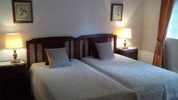 Una cama doble con ropa de cama blanca y un cabecero de madera, dos mesitas de noche con lámparas y un cuadro en la pared.