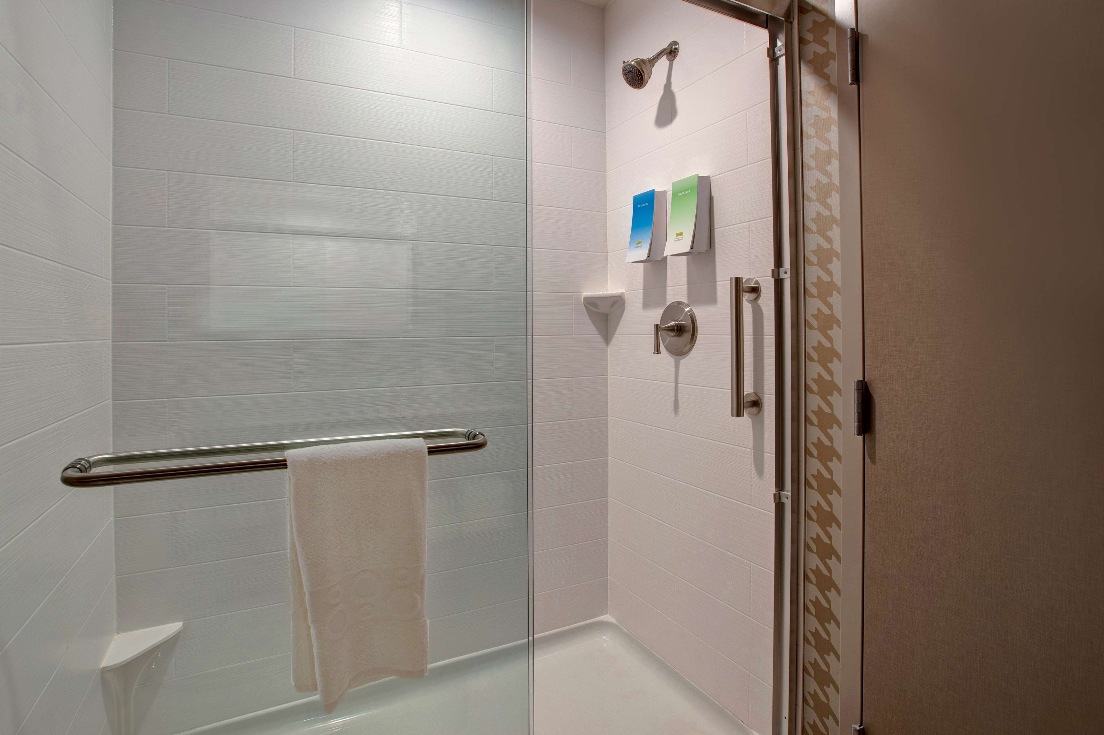 A modern bathroom with white tiled walls, a glass shower enclosure, a towel rack, and a toilet.