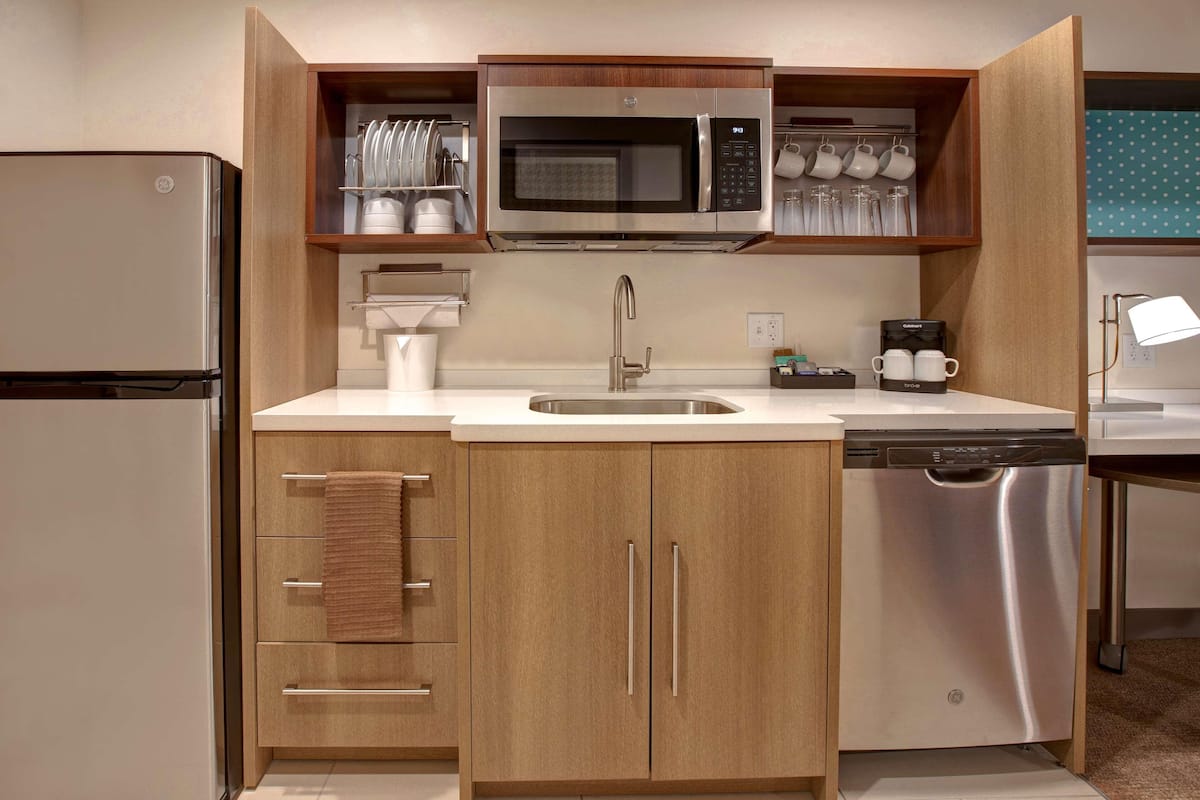 A compact kitchen with a stainless steel refrigerator, a microwave, a dishwasher, and a sink.