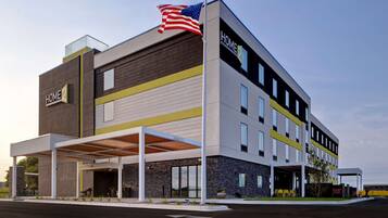 A modern hotel with a flat roof, a covered outdoor area, and a flag on top.