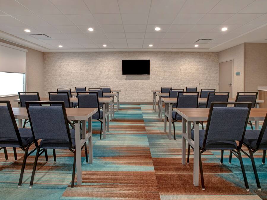 A conference room with a large screen, multiple tables, and chairs arranged for meetings.