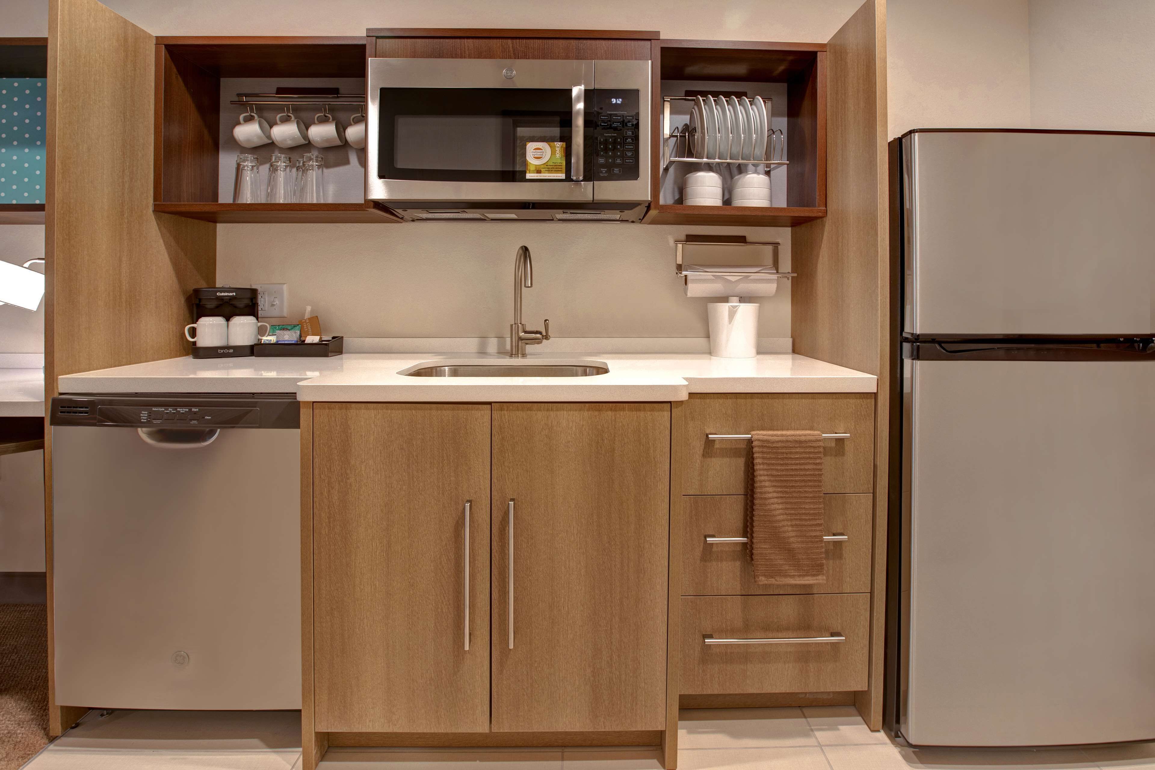 Cocina compacta con microondas integrado, refrigerador de acero inoxidable y lavavajillas.