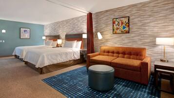 Habitación de hotel con dos camas, un sofá, un puf redondo y una alfombra estampada.