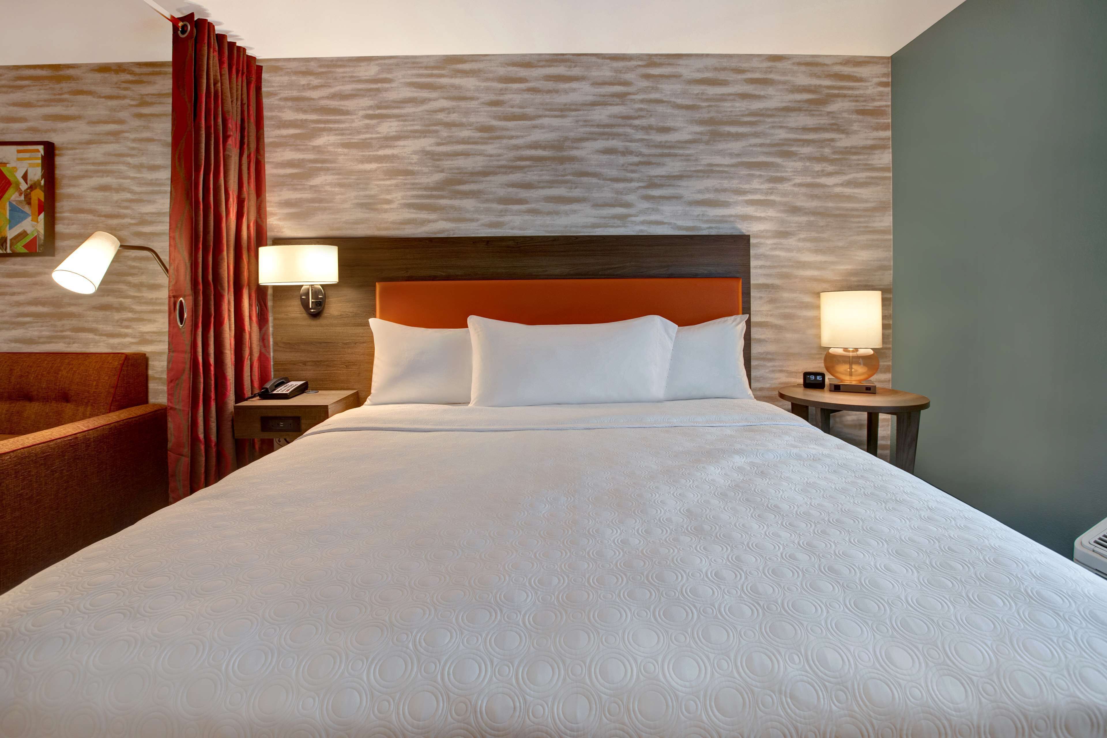 A hotel room with a large bed, two bedside tables with lamps, a wooden headboard, and a red curtain.