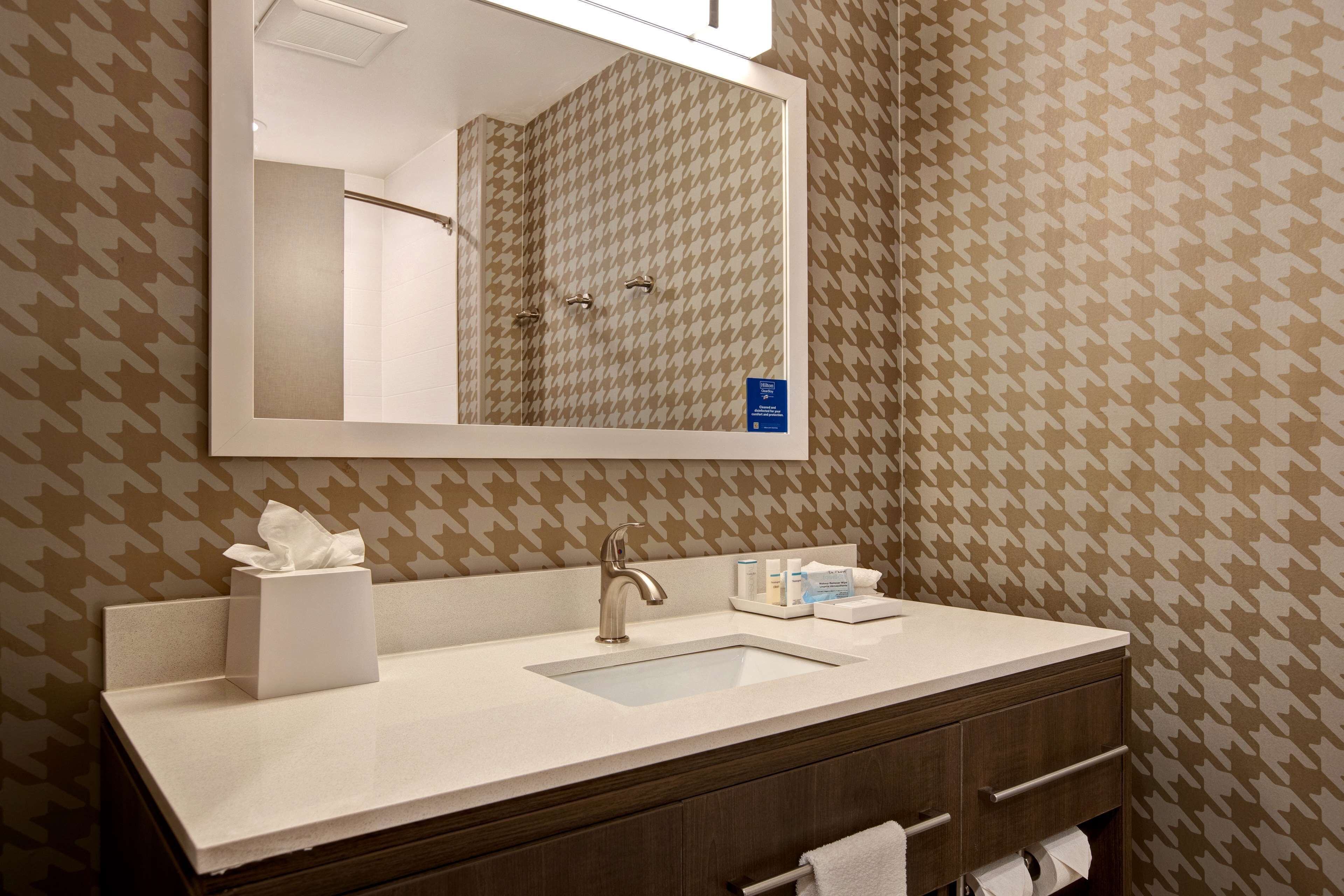 A bathroom with a mirror, sink, towel rack, and toiletries.