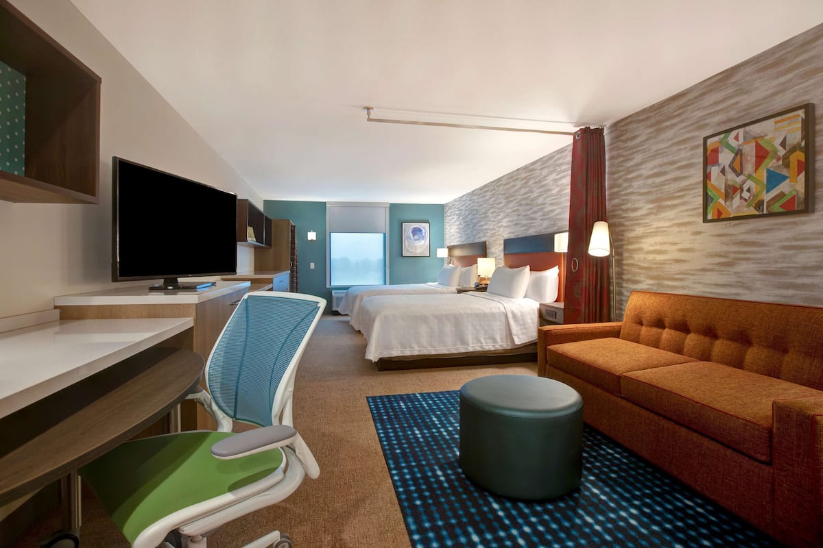 A hotel room with a desk, a bed, a sofa, a TV, and a window.