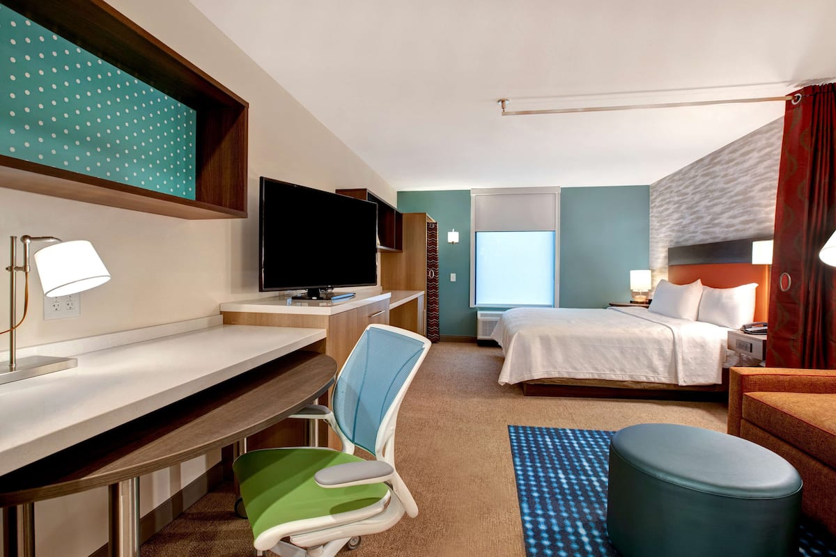 A hotel room with a desk, a television, a bed, a chair, and a small table.