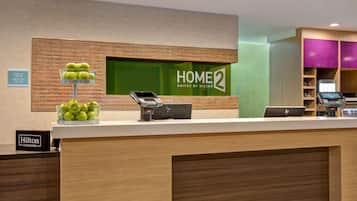 A hotel reception desk with a digital kiosk, a laptop, and a sign indicating check-in times.