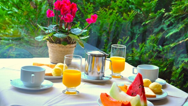 Una mesa de desayuno con una cafetera, dos tazas, una jarra y un plato con fruta.