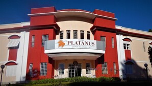 Un hotel llamado "Hotel PlatanuS" con fachada roja y color crema, ventanas grandes y una entrada destacada con un cartel.