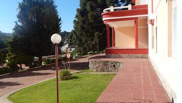 Un edificio con fachada roja y blanca, un paseo empedrado y una zona verde con un farol.