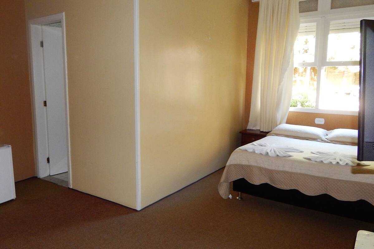 Un dormitorio con cama, mesita de noche, cómoda, puerta y ventana con cortinas.