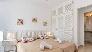 A bedroom with two beds, white headboards, a nightstand with a lamp, and artwork on the wall. - Air-Conditioned Holiday Apartment "Bungalow Cala Dor 27" with Sea View and Pool (Cala D'or)