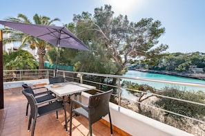 A balcony with a table and chairs, overlooking a coastal view with trees and a body of water.