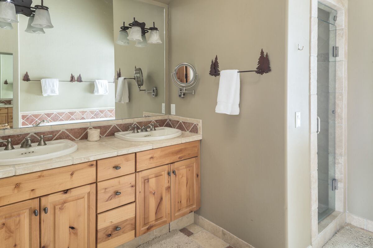 A bathroom with two sinks, wooden cabinets, a mirror, and a glass shower enclosure.