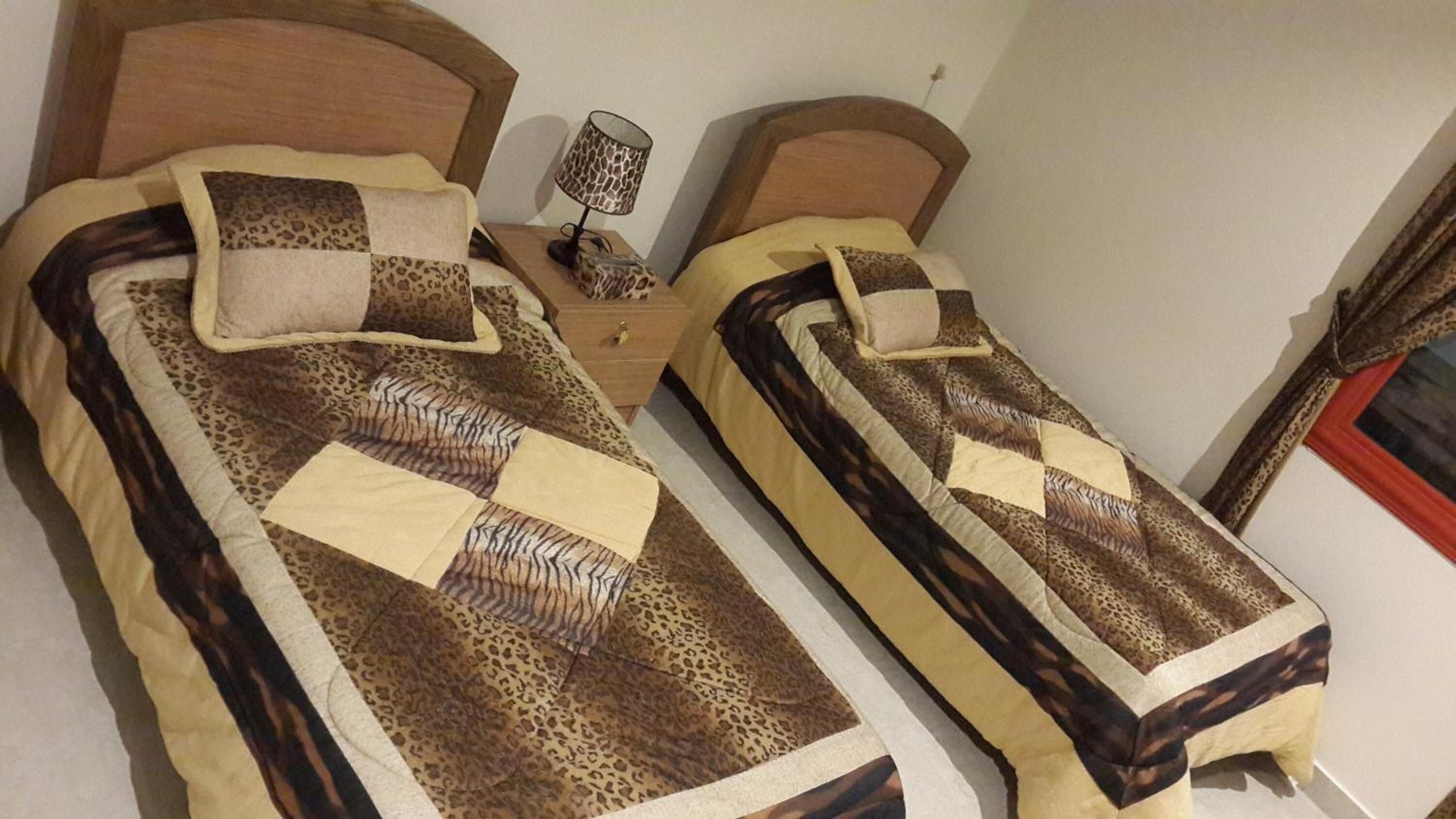 Dos camas individuales con ropa de cama de estampado de leopardo, una mesita de noche con lámpara y un pequeño atril.
