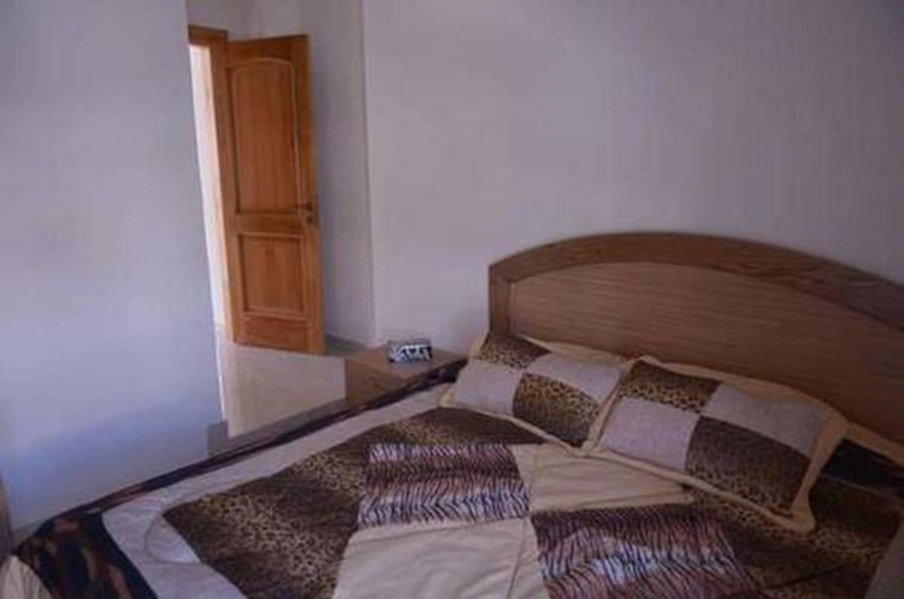 A bedroom with a wooden headboard, a bed with patterned bedding, and a wooden wardrobe.