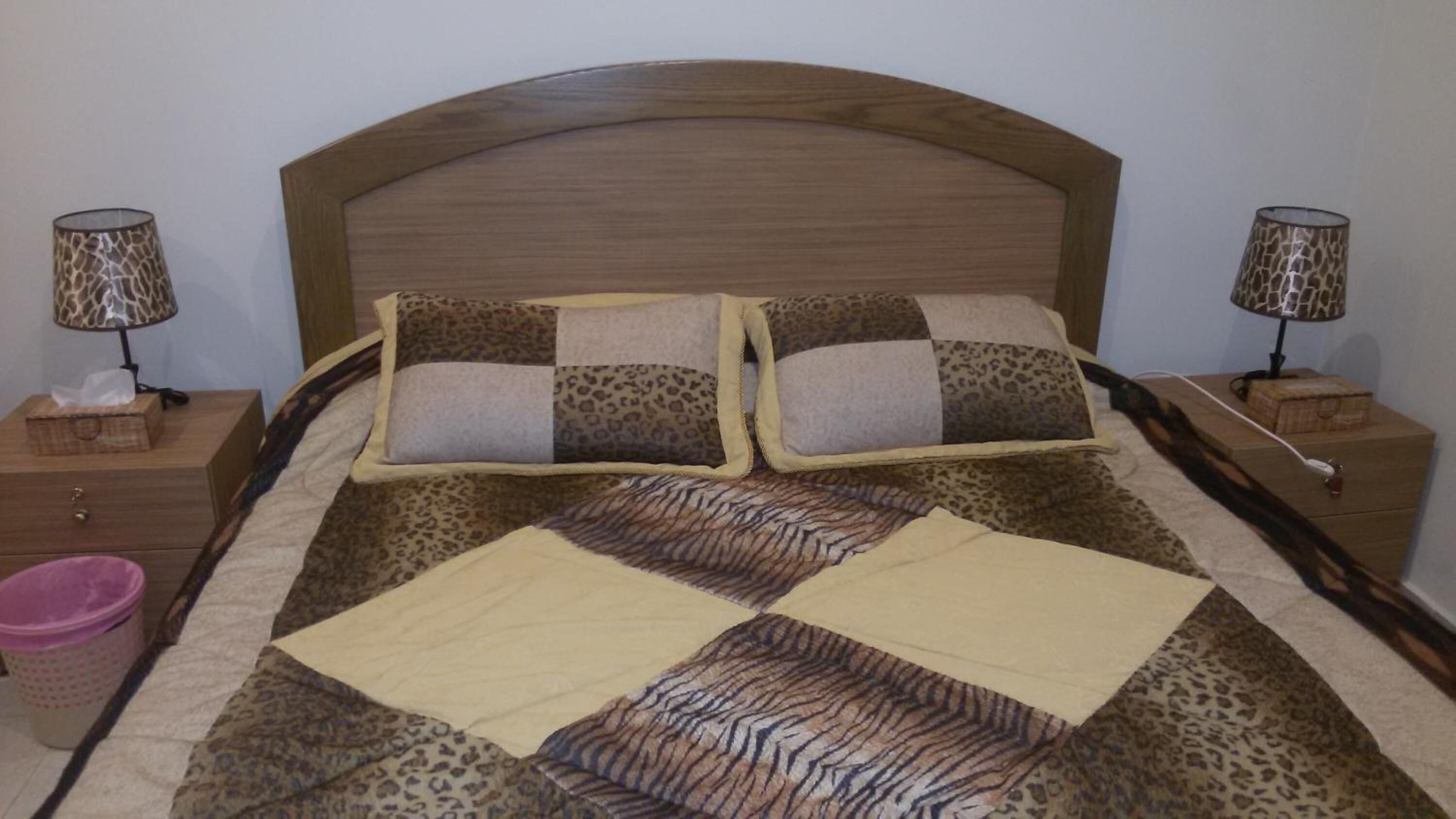 A bed with a leopard print bedspread and two matching pillows, flanked by nightstands with lamps and a tissue box.