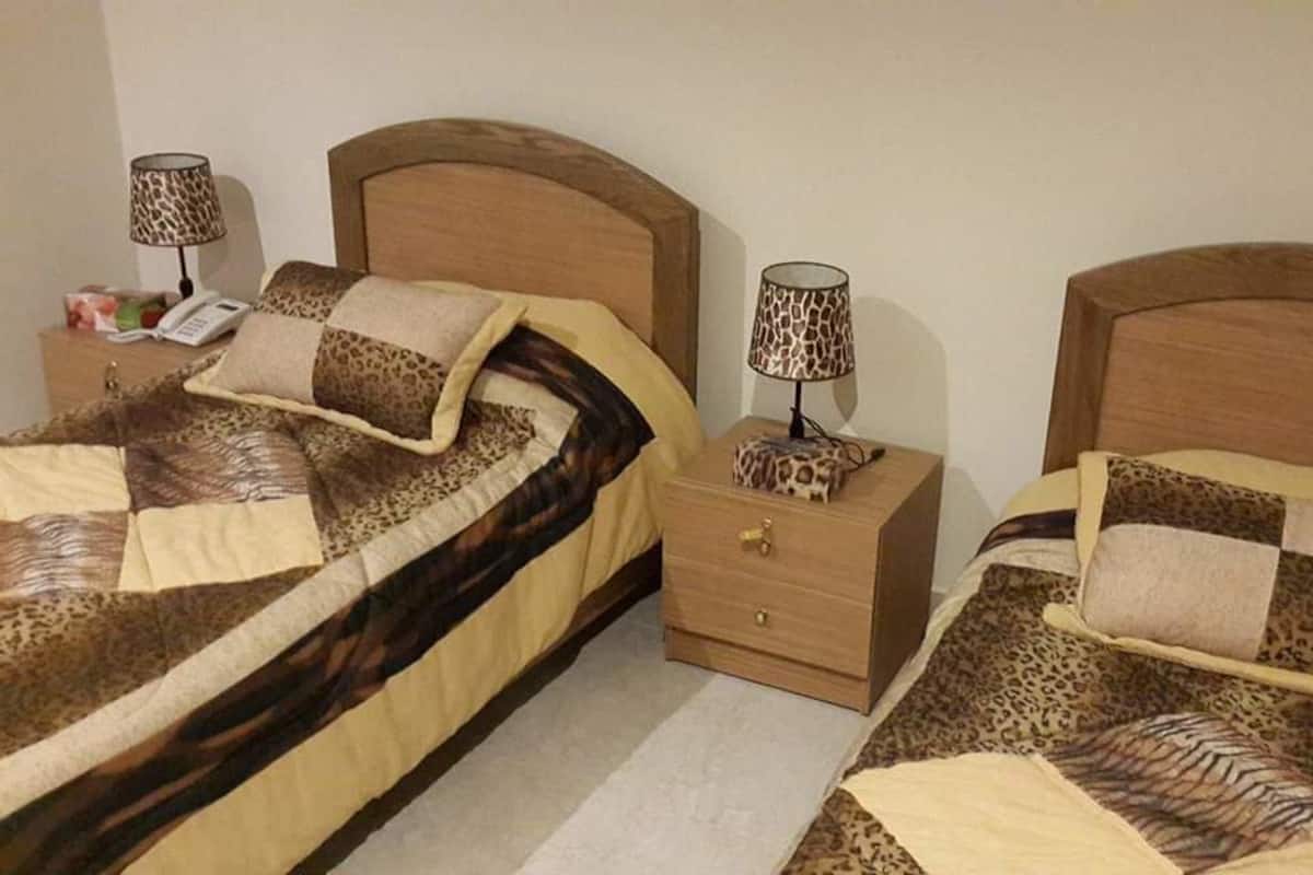 Een slaapkamer met twee bedden, elk voorzien van een houten hoofdbord en een nachtkastje met een lamp.