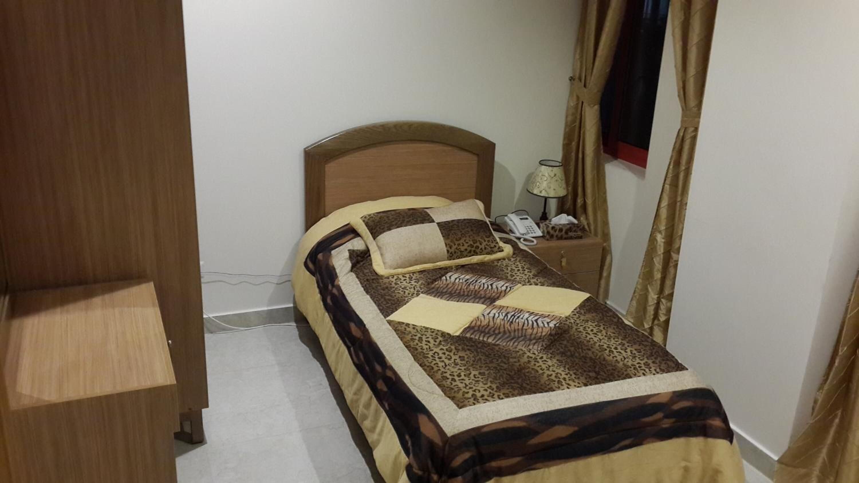 A small, single-bed room with a wooden headboard, a bedside table with a lamp, and a telephone.