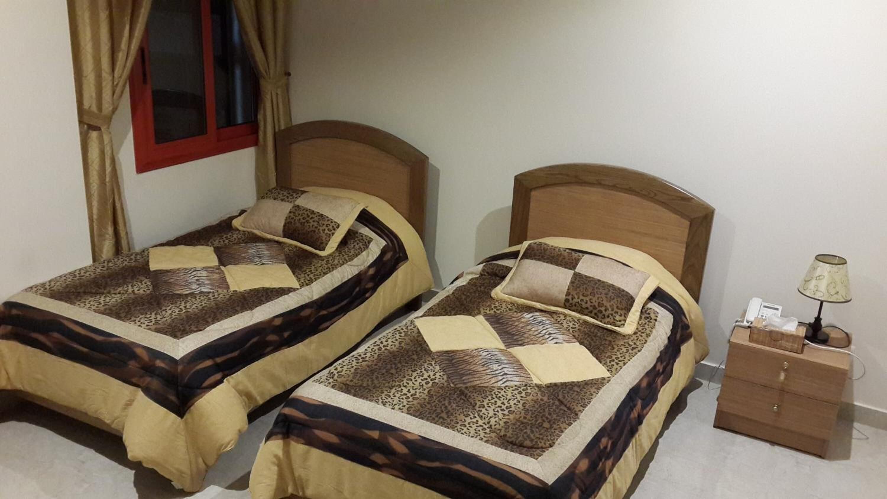 Two single beds with wooden headboards, a bedside table with a lamp, and a window with curtains.
