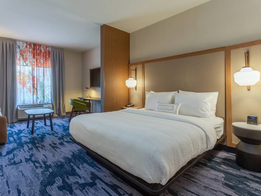 A hotel room with a large bed, a desk, a chair, and a small table.