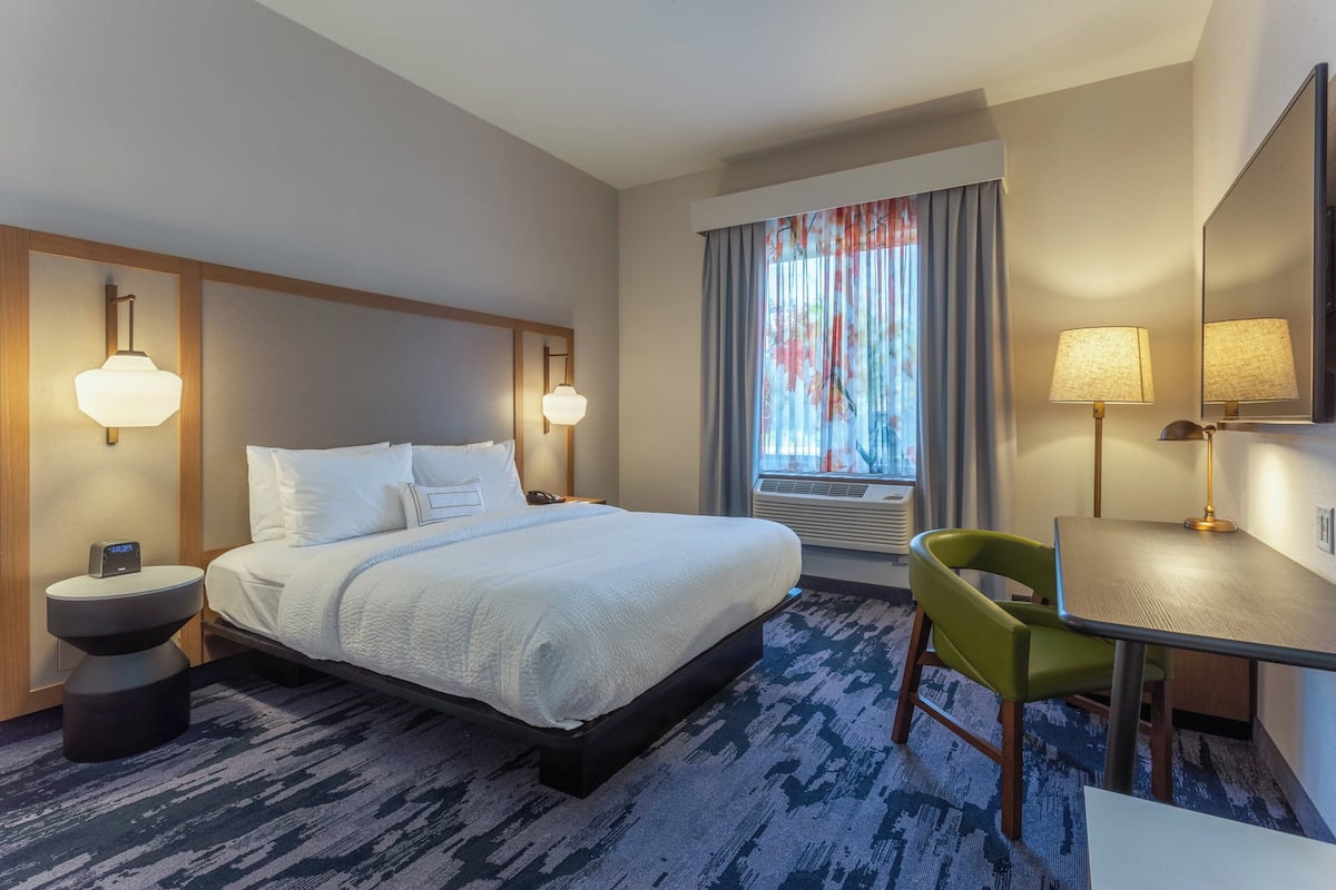 Een hotelkamer met een groot bed, nachtkastjes met lampen, een bureau met stoel en een grote spiegel.