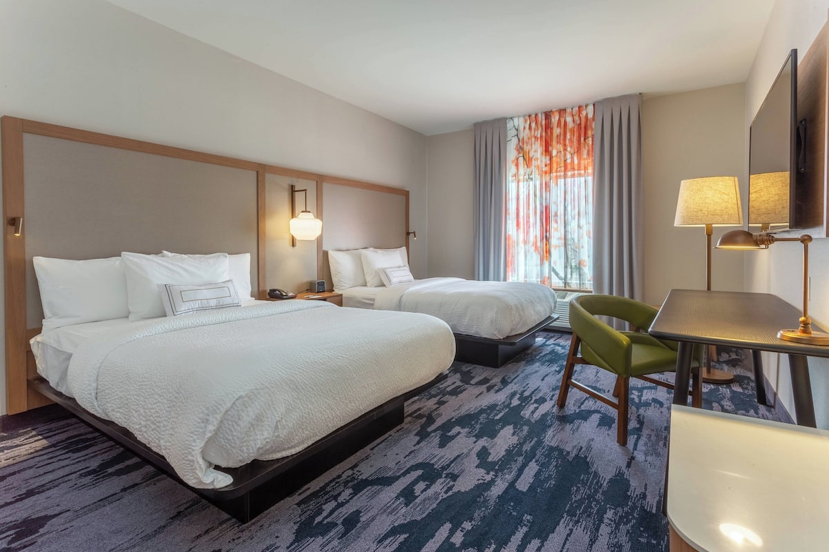 Een hotelkamer met twee bedden, een bureau, een stoel en een groot raam met gordijnen.