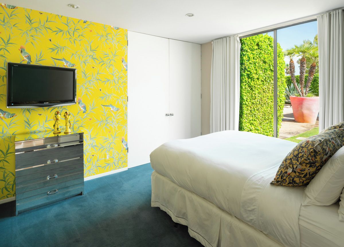 A bedroom with a bed, a dresser, a television, and a view of greenery outside.